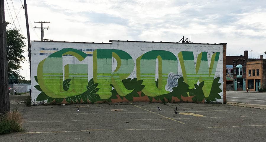 Mural of the word "GROW" painted different shades of green with painted leaves surrounding the bottom of letters.