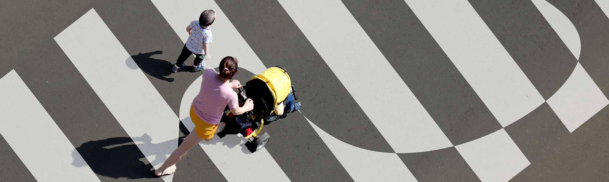 Birds eye view of a child and mother pushing a stroller crossing the street on a cross walk.