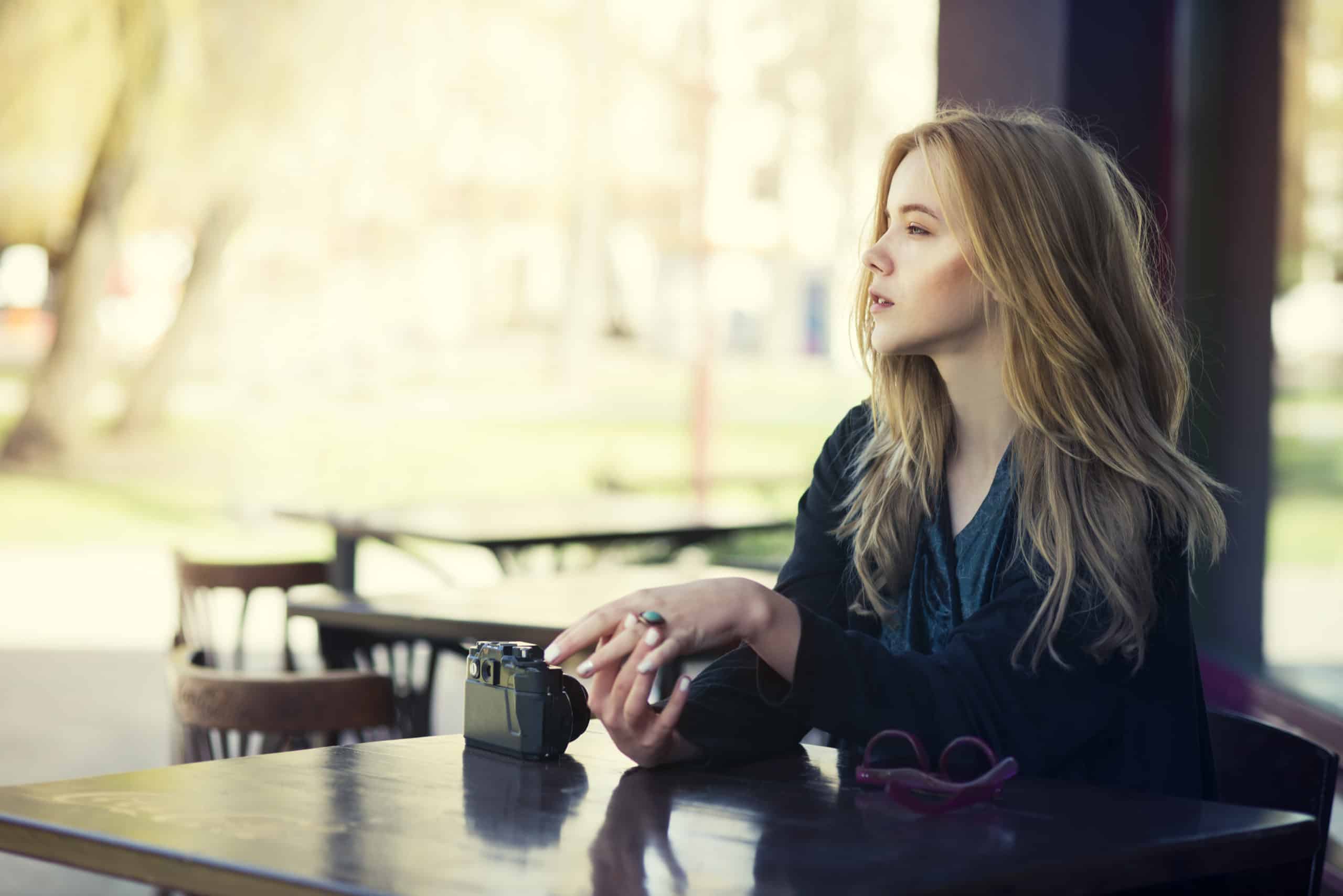 woman sitting at cafe staring longingly out into the street