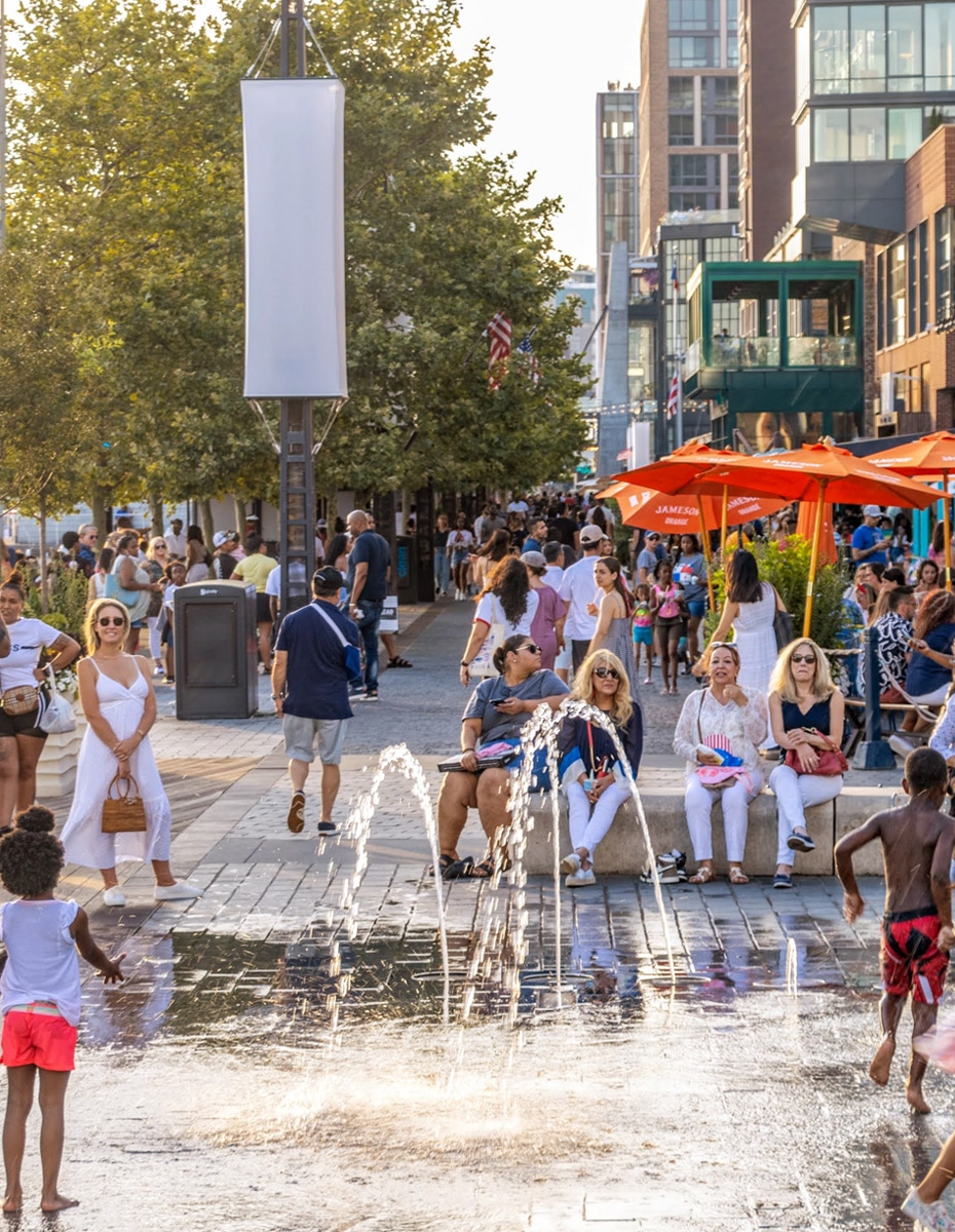 People enjoy an outdoor public sprinkler in a downtown Urban area in the summer.