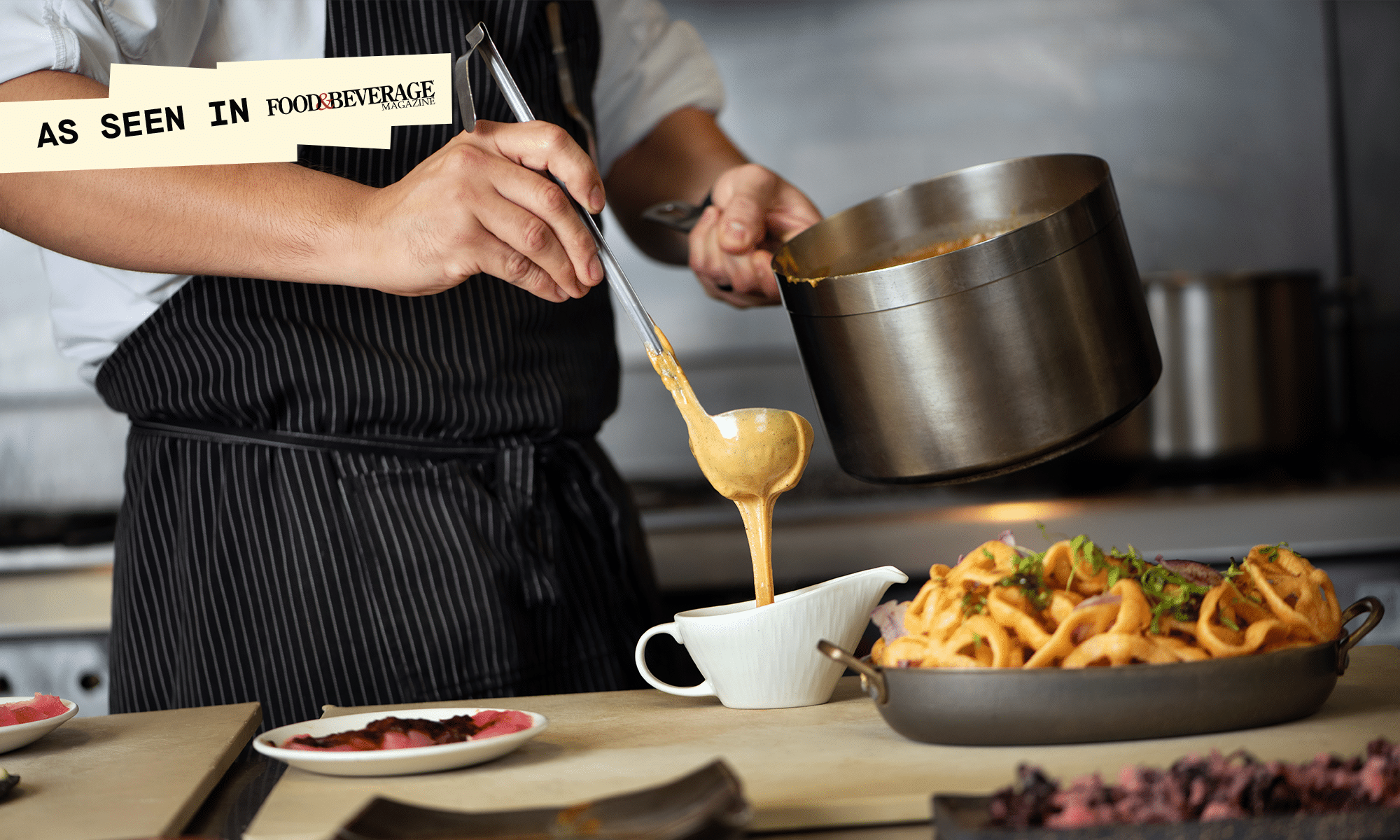 A chef pours hot cheese gravy into a white serving pourer next to an already-prepared dish.