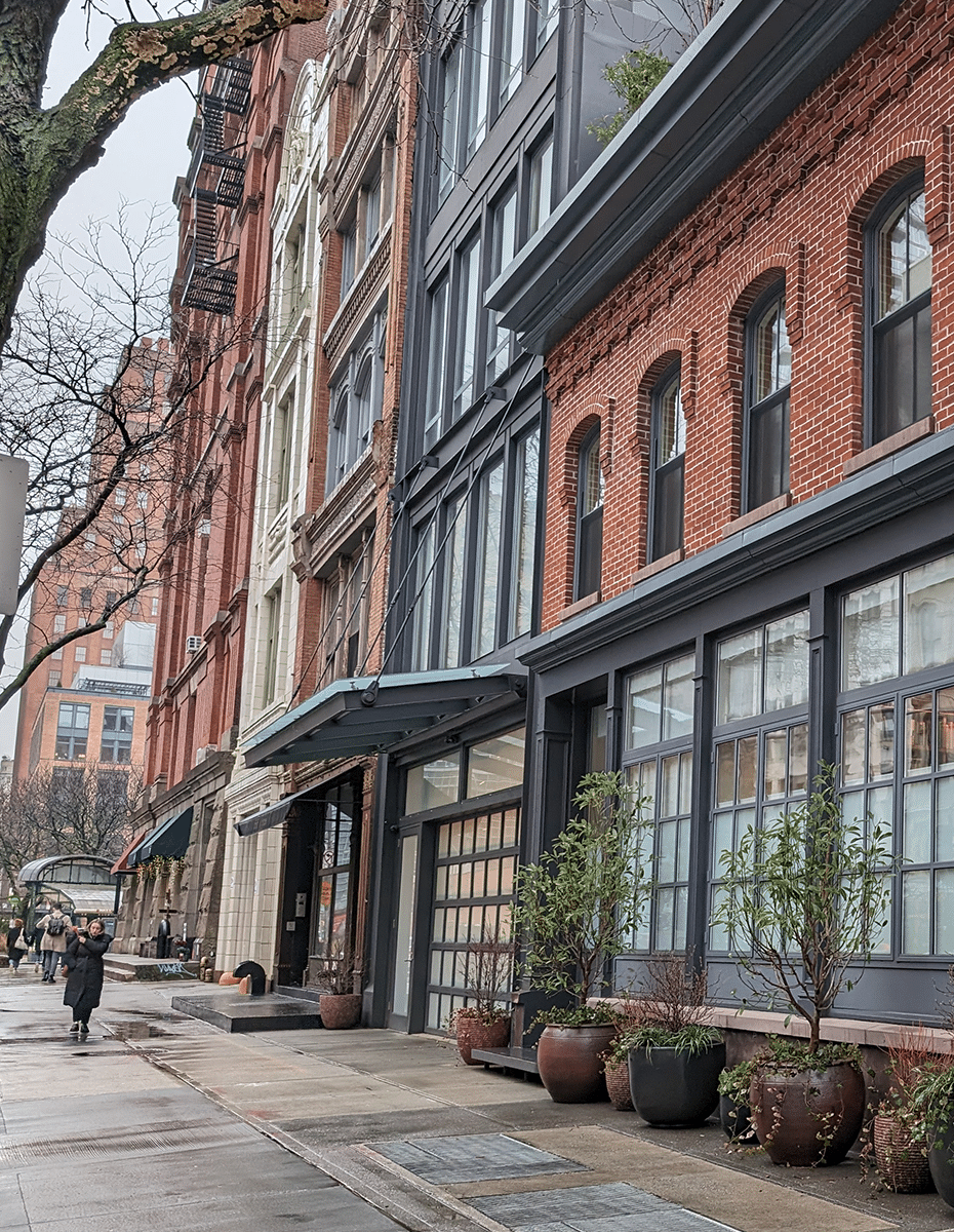 The side of a red brick building with oversized windows in a downtown city area.